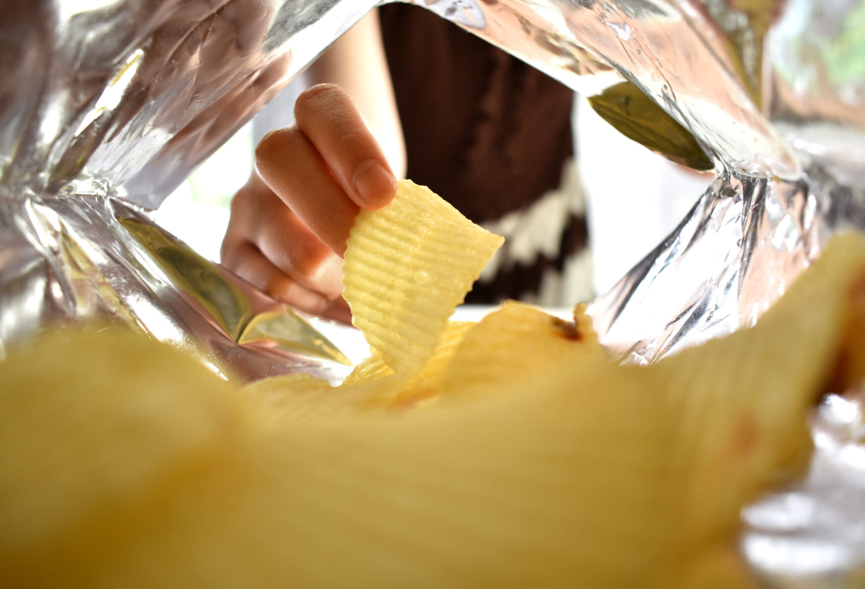 Capital & Main - Woman's hand picking up yellow potato chips inside a bag of snacks.